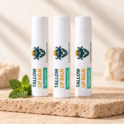 Three Peppermint Tallow Lip Balm tubes on stone beside a mint sprig