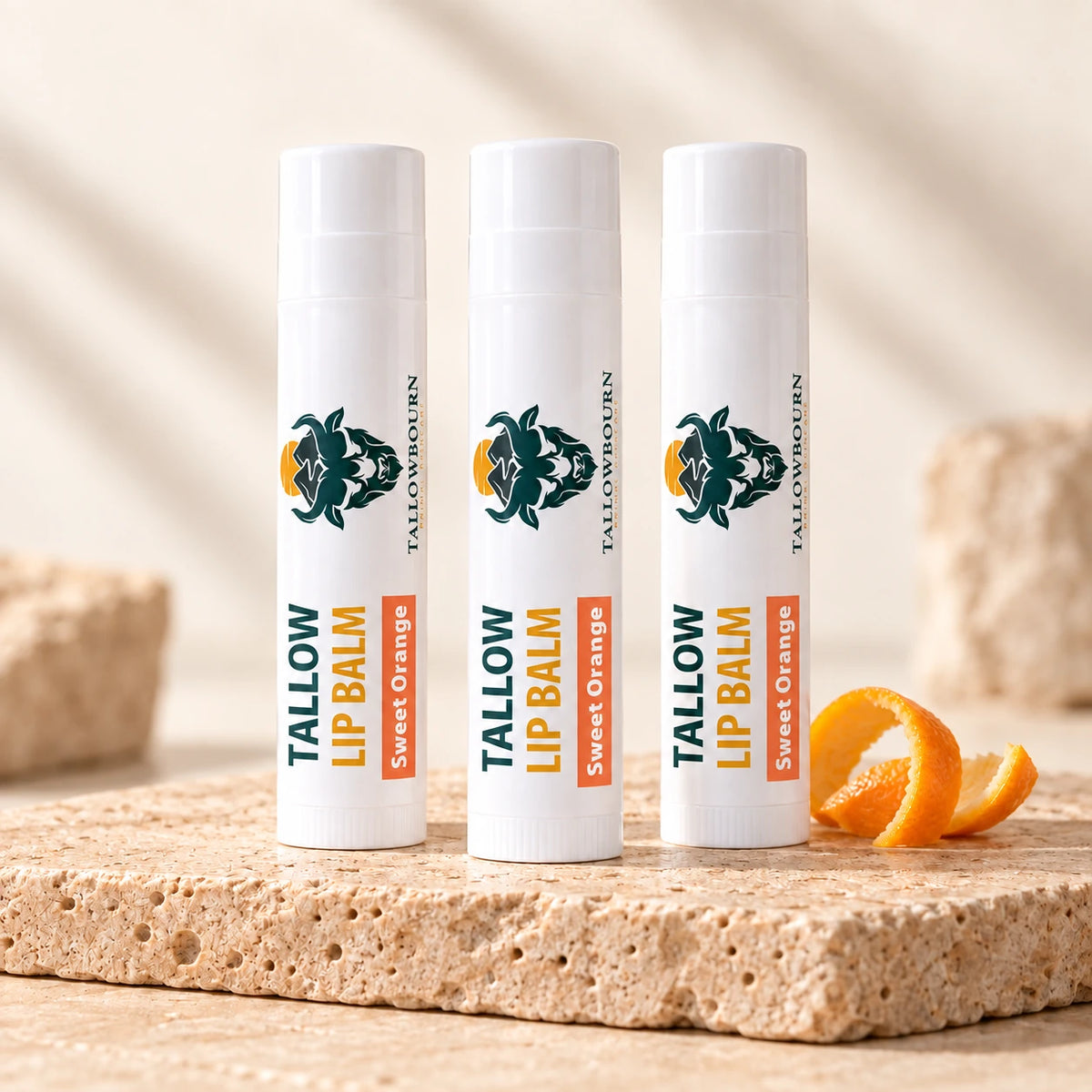 Three Sweet Orange Tallow Lip Balm tubes on stone beside orange peel